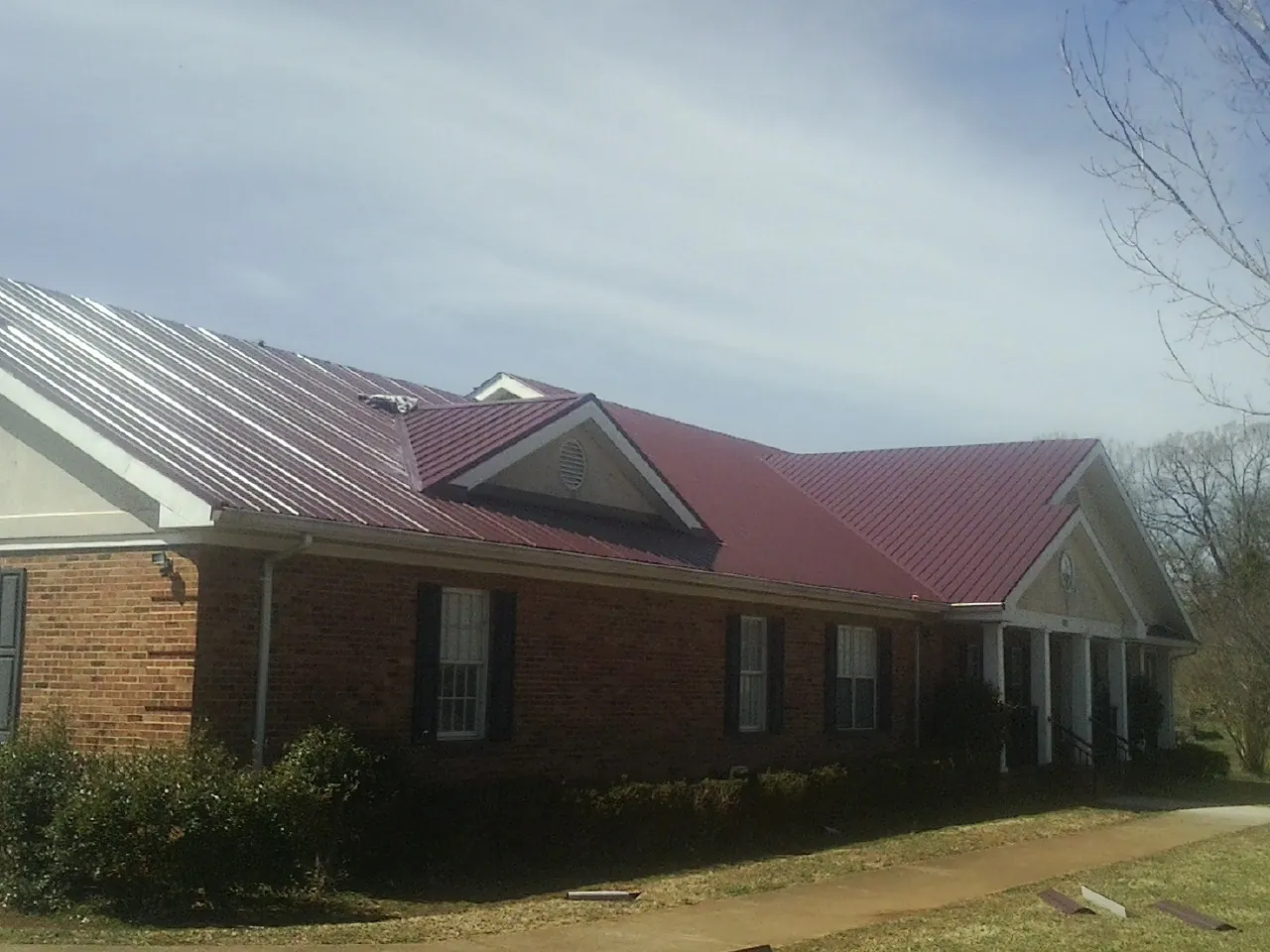 Red metal roof with gabled entries on a long brick building, from a Hail Damage Roof Repair job in Hyrum