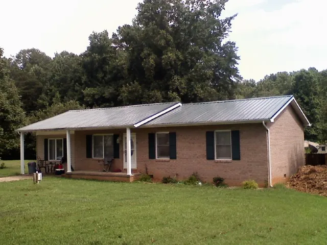 Gray metal roof on a brick ranch house with a side carport in Hyrum