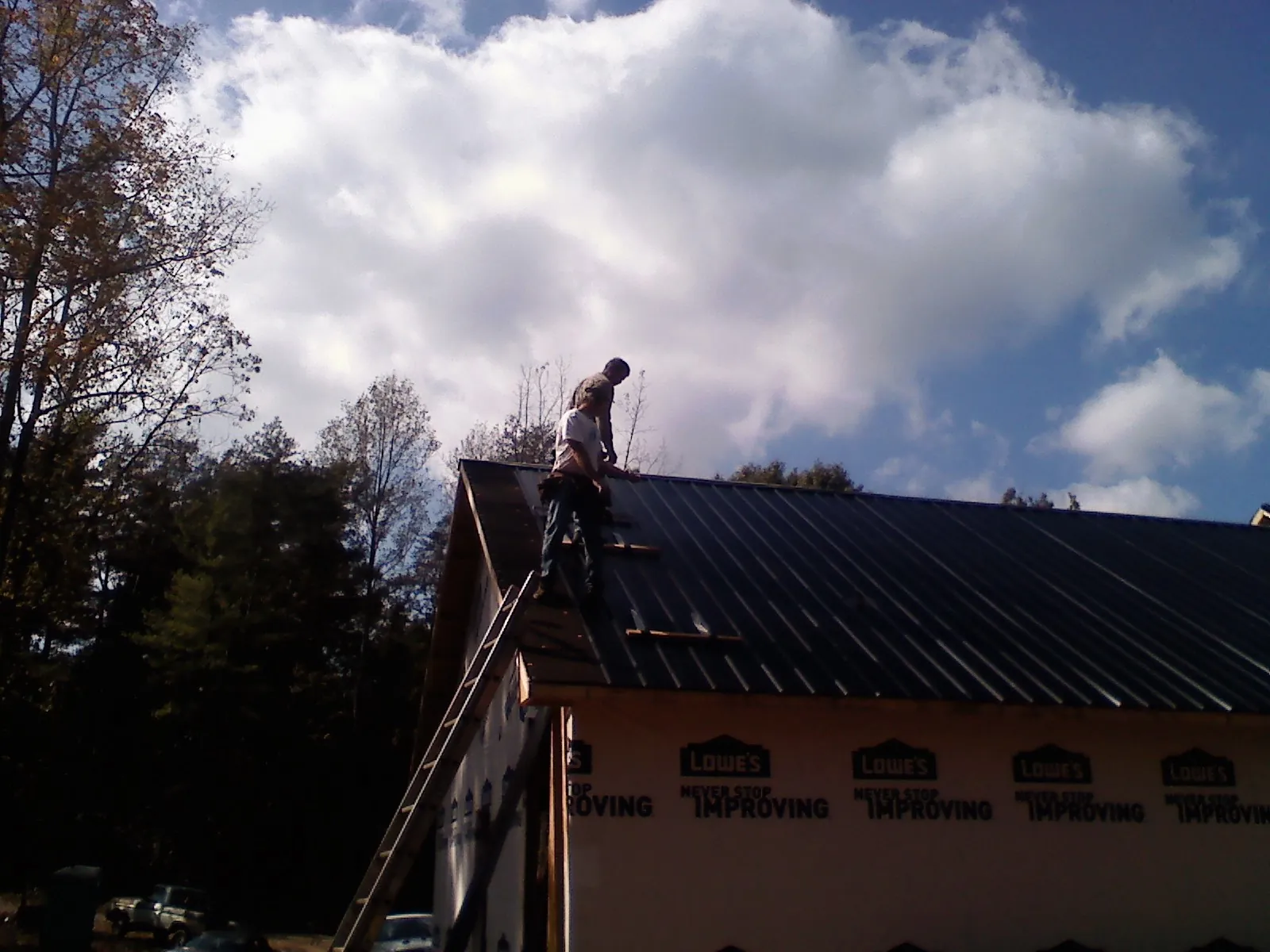Roofer fastening dark metal panels high against a cloudy sky, from a Roof Inspection job in Hyrum