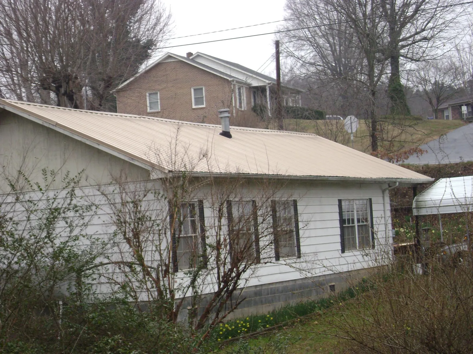 Tan metal roof on a white sided house set into a hillside — Commercial Roofing by Roofing Brothers in Hyrum