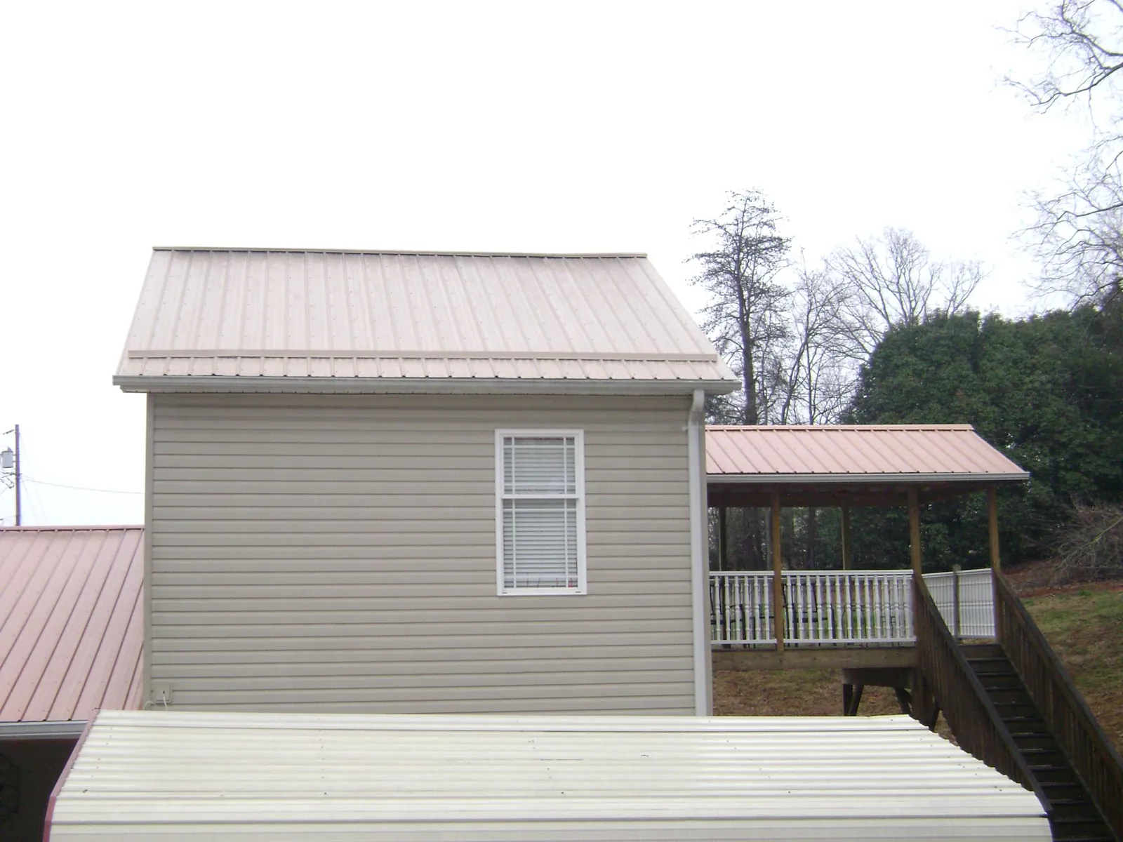 Tan metal roofs on a two story addition and attached porch, from a Roof Replacement job in Hyrum