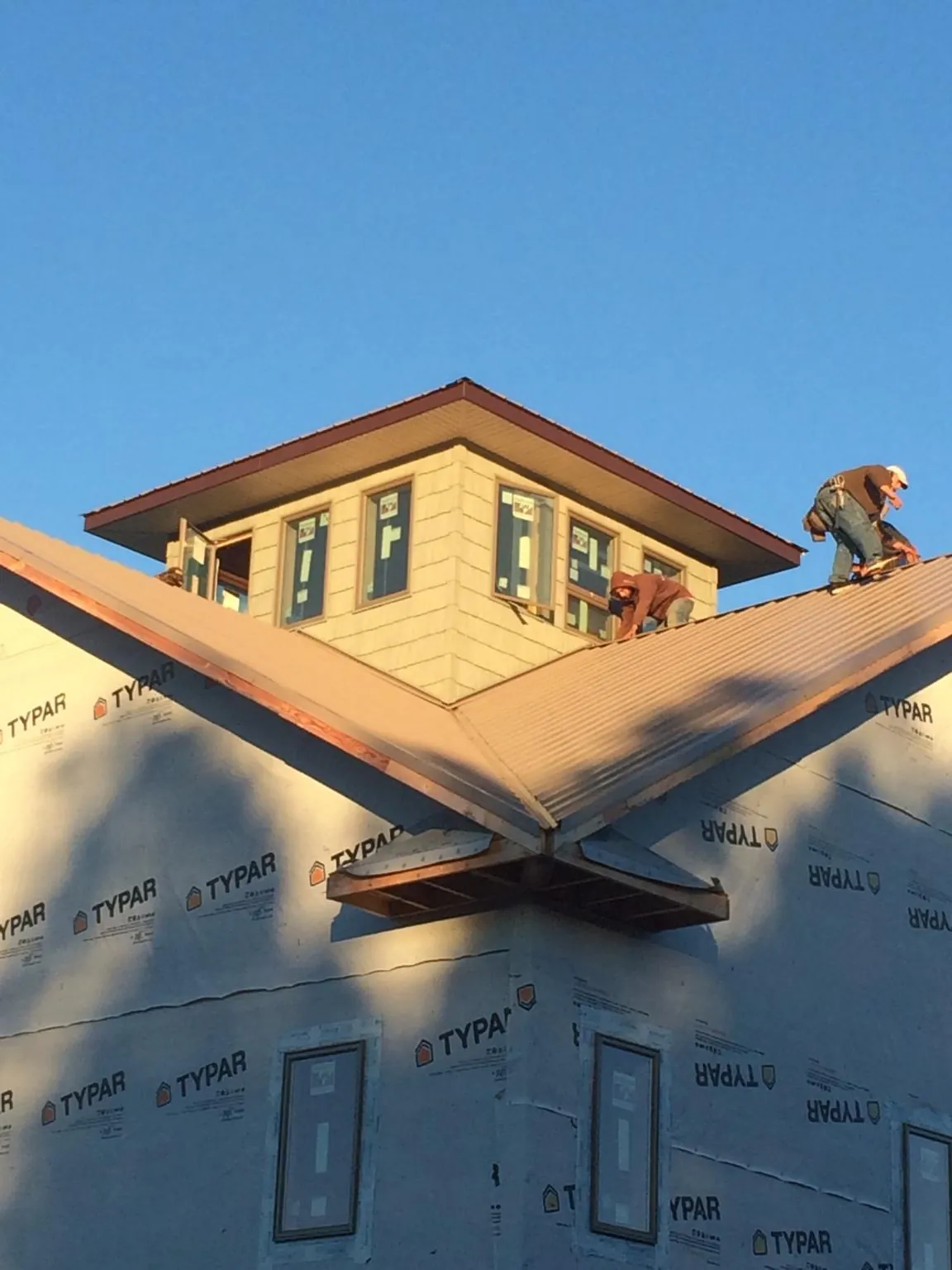 Roofers working around a rooftop cupola on a new metal roof at sunset — Roof Waterproofing in Hyrum by Roofing Brothers